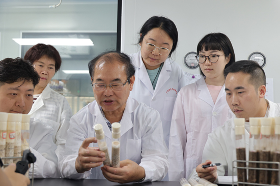 王健在實(shí)驗室里向年輕的科研人員講授怎樣識別不同品種的菌種菌絲生長特點(diǎn)。桂林市委老干部局供圖