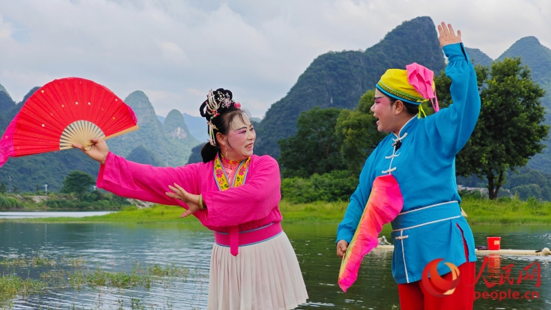 行進中國丨山水搭臺，“快樂劇種”綻華彩手腕輕轉，扇面翻飛，“花旦”林華珍與“小生”林美秀默契配合，將一段黃花腔唱得有聲有色。你來我往，眼波流轉間，農家兒女互訴心事的情景躍然于山水之間。這鮮活的一幕，是永福彩調藝術生生不息的縮影。